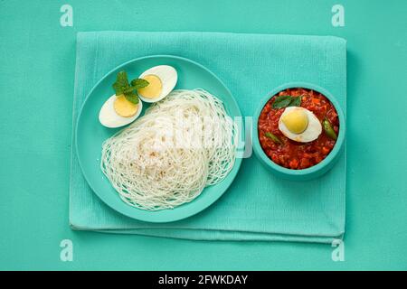 Ideyappam oder Noolappam, südindisches Frühstück, das wunderschön arrangiert ist Mit zwei Scheiben gekochter Eier in aquamarinfarbener Farbe Tafelgeschirr pla Stockfoto