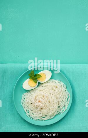 Ideyappam oder Noolappam, südindisches Frühstück, das wunderschön arrangiert ist Mit zwei Scheiben gekochter Eier in aquamarinfarbener Farbe Tafelgeschirr pla Stockfoto