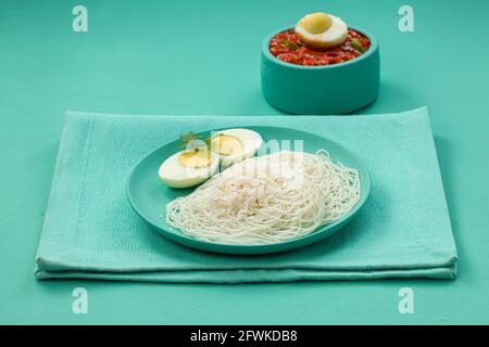 Ideyappam oder Noolappam, südindisches Frühstück, das wunderschön arrangiert ist Mit zwei Scheiben gekochter Eier in aquamarinfarbener Farbe Tafelgeschirr pla Stockfoto