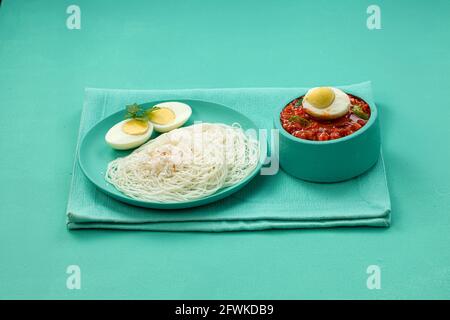 Ideyappam oder Noolappam, südindisches Frühstück, das wunderschön arrangiert ist Mit zwei Scheiben gekochter Eier in aquamarinfarbener Farbe Tafelgeschirr pla Stockfoto