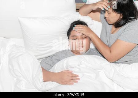 Mutter misst die Temperatur seines kranken Kindes. Krankes Kind mit hohem Fieber liegt im Bett und Mutter fühlt sich gestresst, Gesundheitskonzept. Stockfoto