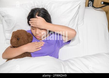 asiatische Kind Mädchen Krankheit auf dem Bett liegen und legte Hand auf die Stirn, um Temperatur zu überprüfen, Health Care Konzept Stockfoto