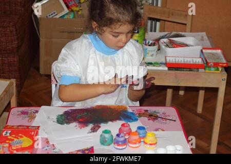 Kleine Malerin mischt neugierig Farben, aber mit ihren Händen statt Palette Stockfoto