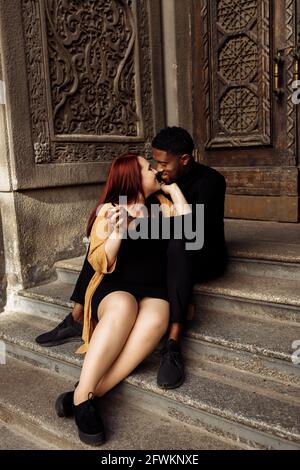 Fröhliches Ehepaar kuschelt in der Nähe des Hauses und lächelt. Fröhlicher afroamerikanischer Mann umarmt sanft schöne kaukasische Frau, genießen Sie Zweisamkeit. Glücklich Stockfoto