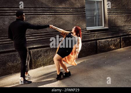 Fröhliches Paar zu Fuß in der Stadt, schöne Frau tanzen mit attraktiven afroamerikanischen Mann, entzückende Frau Spaß mit charmanten Mann, glücklich Stockfoto