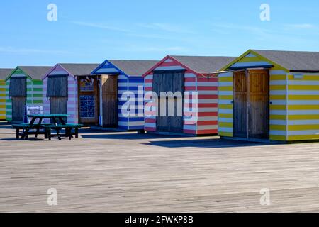 Staycation Idee. Farbenfrohe, gestreifte Strandhütten-Stände in einer Reihe am Hastings Pier, East Sussex, England, Großbritannien. Stockfoto