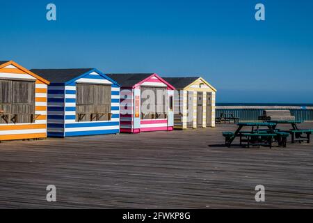 Staycation Idee. Farbenfrohe, gestreifte Strandhütten-Stände in einer Reihe am Hastings Pier, East Sussex, England, Großbritannien. Stockfoto