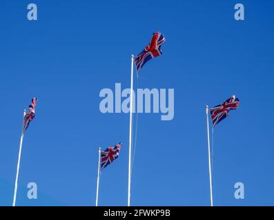 Vier britische Flaggen, die auf Fahnenmasten gegen einen strahlend blauen Himmel im Wind wehen. England. Stockfoto