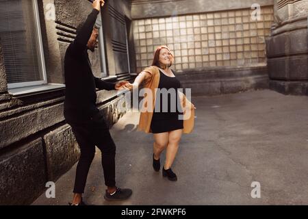 Fröhliches Paar zu Fuß in der Stadt, schöne Frau tanzen mit attraktiven afroamerikanischen Mann, entzückende Frau Spaß mit charmanten Mann, glücklich Stockfoto