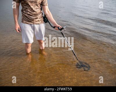 Der Typ im Fluss sucht einen Schatz mit einem Metalldetektor im Wasser. Stockfoto