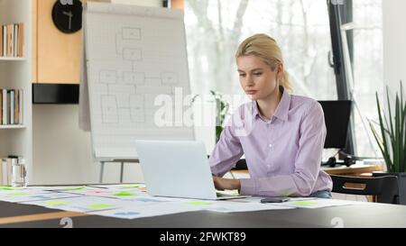 Selbstbewusste junge Geschäftsfrau, die auf einem Laptop am Schreibtisch sitzt Stockfoto