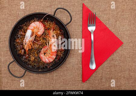 Rezept für Reis, Fisch, Meeresfrüchte und Tintenfisch, gekocht in einer kleinen Paella auf einem Sacktuch. Es gibt zwei große Garnelen und es ist bereit zu essen. Dort Stockfoto