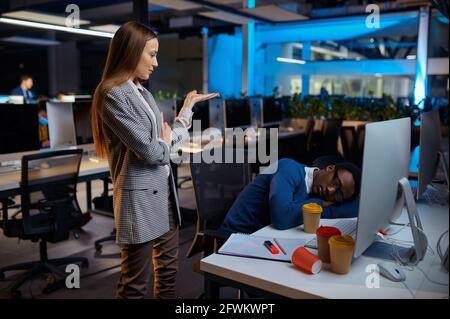 Frau schaut auf den schlafenden Manager, Nachtbüro Stockfoto