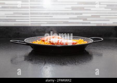 Präsentation in einer Paella eines fertigen Rezeptes von Fideua auf einer Küchenbank. Das Rezept fordert Brühe, dicke Nudeln, Fisch, Tintenfisch, Schalentiere, Garnelen, Stockfoto