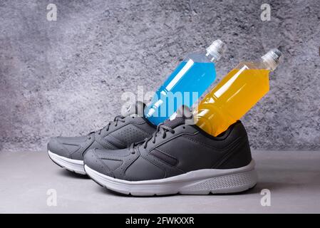 Graue Turnschuhe und zwei Flaschen isotonisches Getränk auf grauem Hintergrund, gesundes Getränk für das Training, Nahaufnahme. Stockfoto