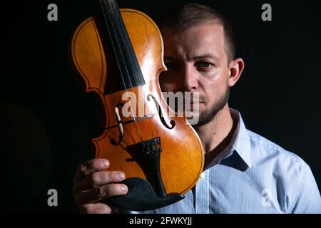 Porträt eines Mannes mit einer Geige in den Händen auf schwarzem Hintergrund. Stockfoto