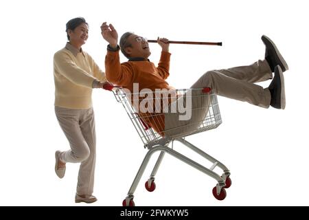 Ein glücklicher alter Mann schiebt seine Frau saß in der Warenkorb Stockfoto