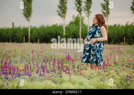 Schwangerschaft und Mutterschaft. Junge Frau erwartet ein Baby, glücklich, Spaß mit ihren zukünftigen Babyschuhen zu haben, halten und auf der Wiese stehen Stockfoto