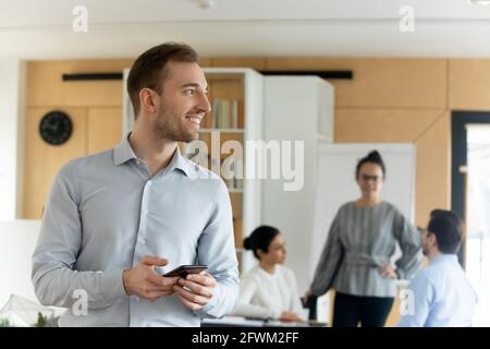 Lächelnder, selbstbewusster, verträumter kaukasischer junger Geschäftsmann lenkte vom Telefon ab Stockfoto