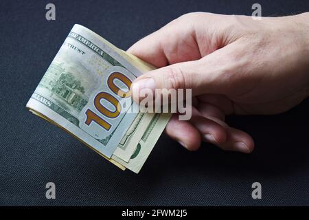 Ein Haufen zusammengerollter Dollarscheine, die in der Hand des kaukasischen Mannes geklammert wurden. Männer halten Bargeldwährung der Vereinigten Staaten auf grauem Hintergrund. Stockfoto