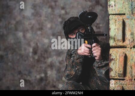 Junger Mann spielt Paintball-Kampfspiel mit seinen Freunden, trägt Tarnung und Schutzmaske, Banner, Freizeitaktivitäten Stockfoto