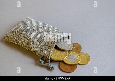 Metallmünzen aus der Tasche auf grauem Hintergrund verstreut. Konzept der Speicherung von Geld. Materialsack mit Geld. Münzen aus verschiedenen Ländern in Beutel gesammelt. Stockfoto