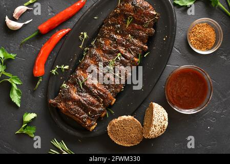 Gegrillte Spareribs auf die Platte über der schwarzen Stein Hintergrund. Leckere bbq-Fleisch. Ansicht von oben, flach Stockfoto