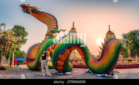 Regenbogenschnitzelschlange oder bunte Thai Naga und asiatische Frau stehen im Sonnenuntergang am Wat Phra That Nong Bua Tempel, Ubon Ratchathani Stockfoto