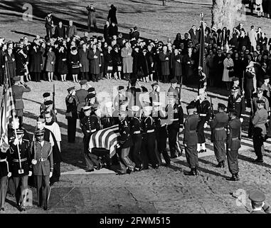 Ehrengäste tragen die Fahnenschatulle von Präsident John F. Kennedy zum Grab auf dem Arlington National Cemetery, während der Trauerfeier am Grab des Staatspräsidenten Kennedy. In Prozession: Erzbischof von Washington, Patrick A. O’Boyle; Vorsitzender der Generalstabschefs, General Maxwell D. Taylor; Stabschef der United States Air Force, General Curtis E. LeMay. Beamte und Würdenträger beobachten, darunter Senator Kenneth B. Keating (New York); Senator Daniel Inouye (Hawaii). Stockfoto