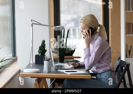 Seitenansicht selbstbewusste Geschäftsfrau, die mit einem Laptop telefoniert Stockfoto