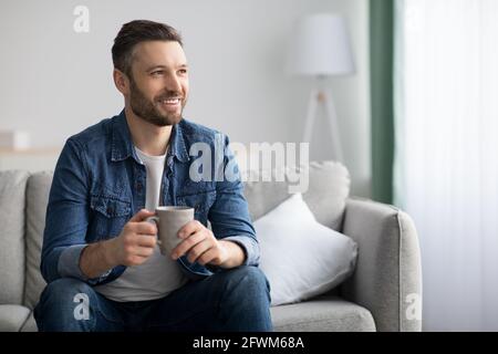 Fröhlicher bärtiger Mann, der zu Hause eine Tasse Kaffee genießt Stockfoto
