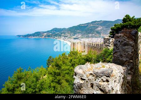 Schöne Aussicht auf die Stadt Alanya von oben. Eine alte Verteidigungsmauer, die in grünen Bäumen begraben ist, und ein Ferienort, der von einem blauen Meer auf einem si umgeben ist Stockfoto