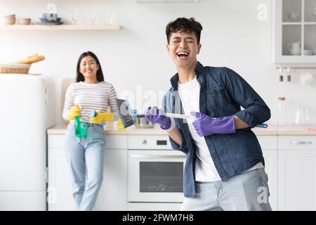 Lustige asiatische Kerl imitieren Rockstar beim Reinigen der Küche Stockfoto