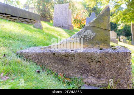 Ein alter gebrochener Grabstein auf der Seite eines kleinen Hügels in einem Friedhof. Nur ein kleiner Teil des unteren Teils des Grabmarkers bleibt erhalten. Nahaufnahme. Stockfoto