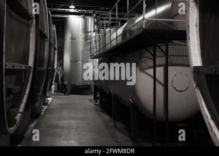 Dunkle Holzfässer und Stahltanks befinden sich in einem Keller der Weinkellerei, Nahaufnahme mit selektivem Fokus Stockfoto