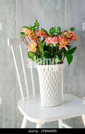 Blumenstrauß aus Dahlia in Keramikvase, stehend auf weißem Holzstuhl. Grauer Steinhintergrund. Stockfoto