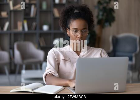 Konzentrierte junge afrikanische Frau in Brillen, die am Computer arbeiten. Stockfoto