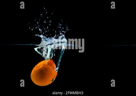 Mandarin fällt ins Wasser und erzeugt auf schwarzem Hintergrund Spray, Kopierfläche Stockfoto
