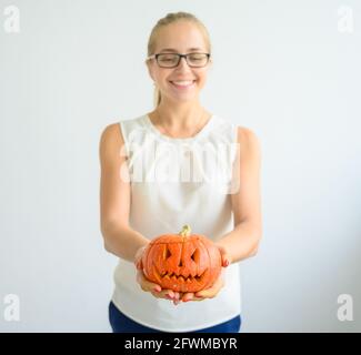Eine Frau in einer weißen Bluse hält einen Kürbis für Halloween. Nahaufnahme von weiblichen Händen mit einem Laterne Bube auf weißem Hintergrund am Vorabend von Allerheiligen Stockfoto