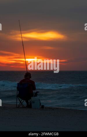 Ein Mann fischt bei Sonnenaufgang auf der Assateague Island National Seashore in der Brandung. Stockfoto