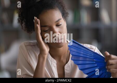 Erschöpfte überhitzte junge afrikanische Frau winkend Papierfächer. Stockfoto