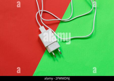 Weißes Telefonladegerät isoliert auf halbrotem, halbgrünem Hintergrund. Technologische Geräte. Stockfoto