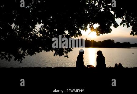 Hannover, Deutschland. Mai 2021. Sophie (l.) und Marleen sitzen in der untergehenden Sonne auf einer Wand am Maschsee und unterhalten sich. Quelle: Hauke-Christian Dittrich/dpa/Alamy Live News Stockfoto