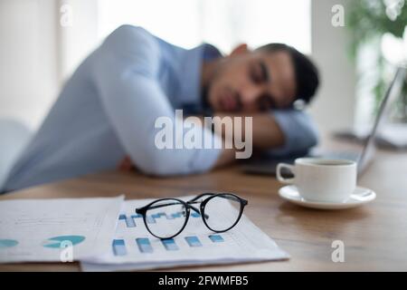 Erschöpfter arabischer Geschäftsmann, der auf seinem Schreibtisch schläft, müde von Überarbeit, selektiver Konzentration auf Dokumente und Brille Stockfoto