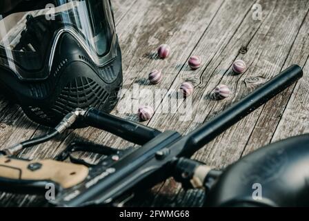 Nahaufnahme der Paintball-Pistole, spezielle Kugeln und Schutzmaske, Ausrüstung zum Spielen von Paintball auf einem Holztisch, Action-Spiel-Konzept Stockfoto