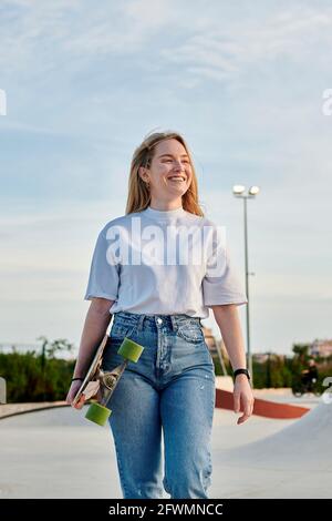 Junge blonde Frau lächelt und hat Spaß mit einem Skateboard Stockfoto