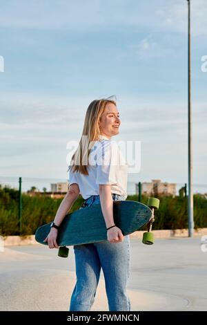 Junge blonde Frau lächelt und hat Spaß mit einem Skateboard Stockfoto