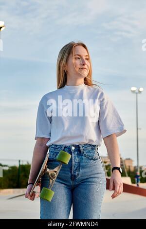 Junge blonde Frau lächelt und hat Spaß mit einem Skateboard Stockfoto
