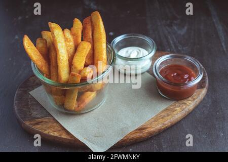 Pommes frites in einer Glasschüssel auf einem Holzboden serviert Platine Stockfoto