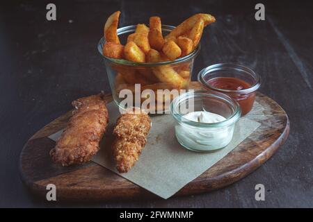 Zwei Hähnchenstreifen im Teig mit pommes frites auf einem Holzbrett Stockfoto